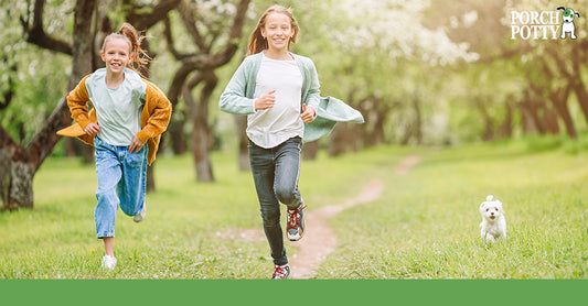 Two children run in their yard, a small white dog running beside them.